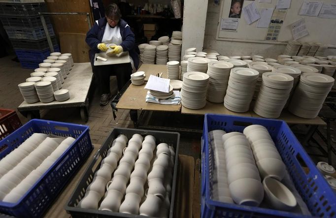 A worker uses a polishing stone on a plate, as she sits amongst trays of partially fired pottery in the "biscuit room" at the Middleport pottery in Stoke-on-Trent, central England January 22, 2013. The pottery which dates back to 1888 and was rescued from closure in 2009, continues to use traditional methods to produce its range of ceramics and famous Burleigh Ware pottery. REUTERS/Phil Noble (BRITAIN - Tags: BUSINESS EMPLOYMENT SOCIETY) Published: Led. 22, 2013, 5:22 odp.