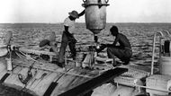 Spolukonstruktér Trieste Jacques Piccard (vpravo) dohlíží na nakládku kovové zátěže. Hlavním konstruktérem byl Piccardův otec August. Snímek byl pořízen během jednoho z testovacích ponorů, které rekordu předcházely. 15. listopad 1959.