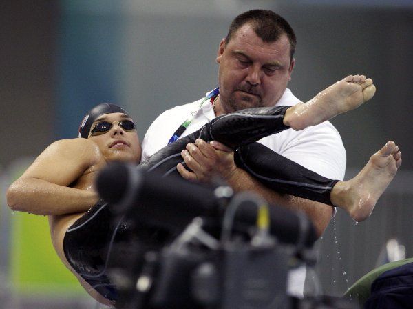 Asistent odnáší z bazénu vítěze závodu na 200 m volným způsobem, Rusa Dmitrije Kokareva.