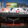 Woman walks past a mural of a pair of wings, under another mural depicting former North Korean leader Kim Jong Il and former South Korean president Kim Dae-jung, hanging above Dan Sung Sa restaurant a
