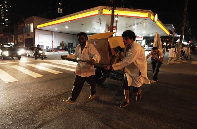 Members of the Traffic Psychologists perform as they help a man to push a cart loaded with cardboard in front of a traffic light in Sao Paulo July 23, 2012. Traffic Psychologists is a non-profit non-governmental organization which aims to humanize traffic and reduce the level of stress caused to drivers. Sao Paulo has more than 7 million vehicles, according to figures from the state transport authority Detran. Picture taken July 23, 2012. REUTERS/Nacho Doce (BRAZIL - Tags: TRANSPORT SOCIETY) Published: Čec. 24, 2012, 7:24 dop.