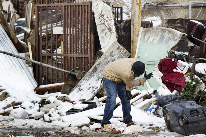 Muž oprašuje sníh ze zbytků poničených věcí. Rockaway Park, New York