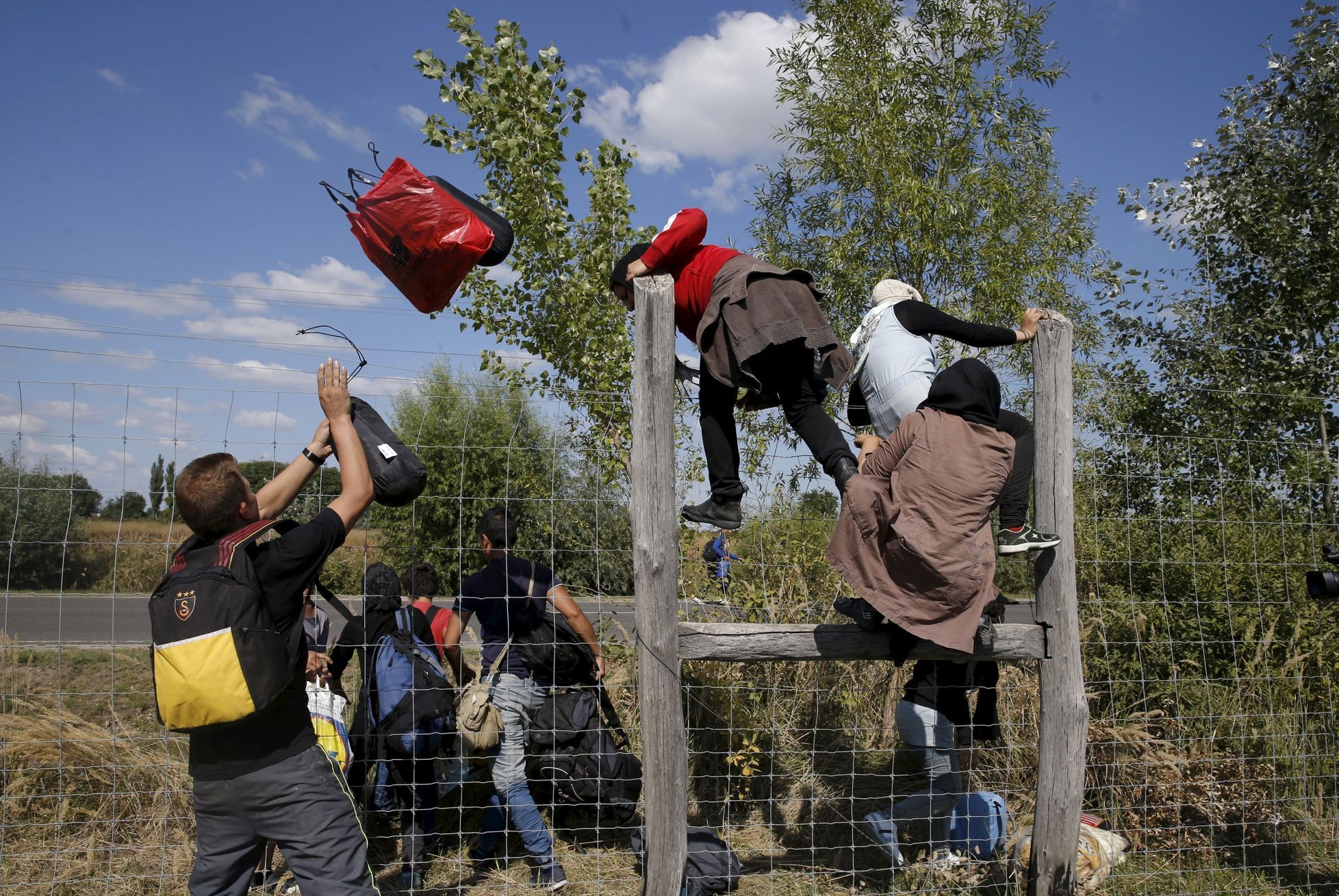 Uprchlíci v Maďarsku přelézají ploty.