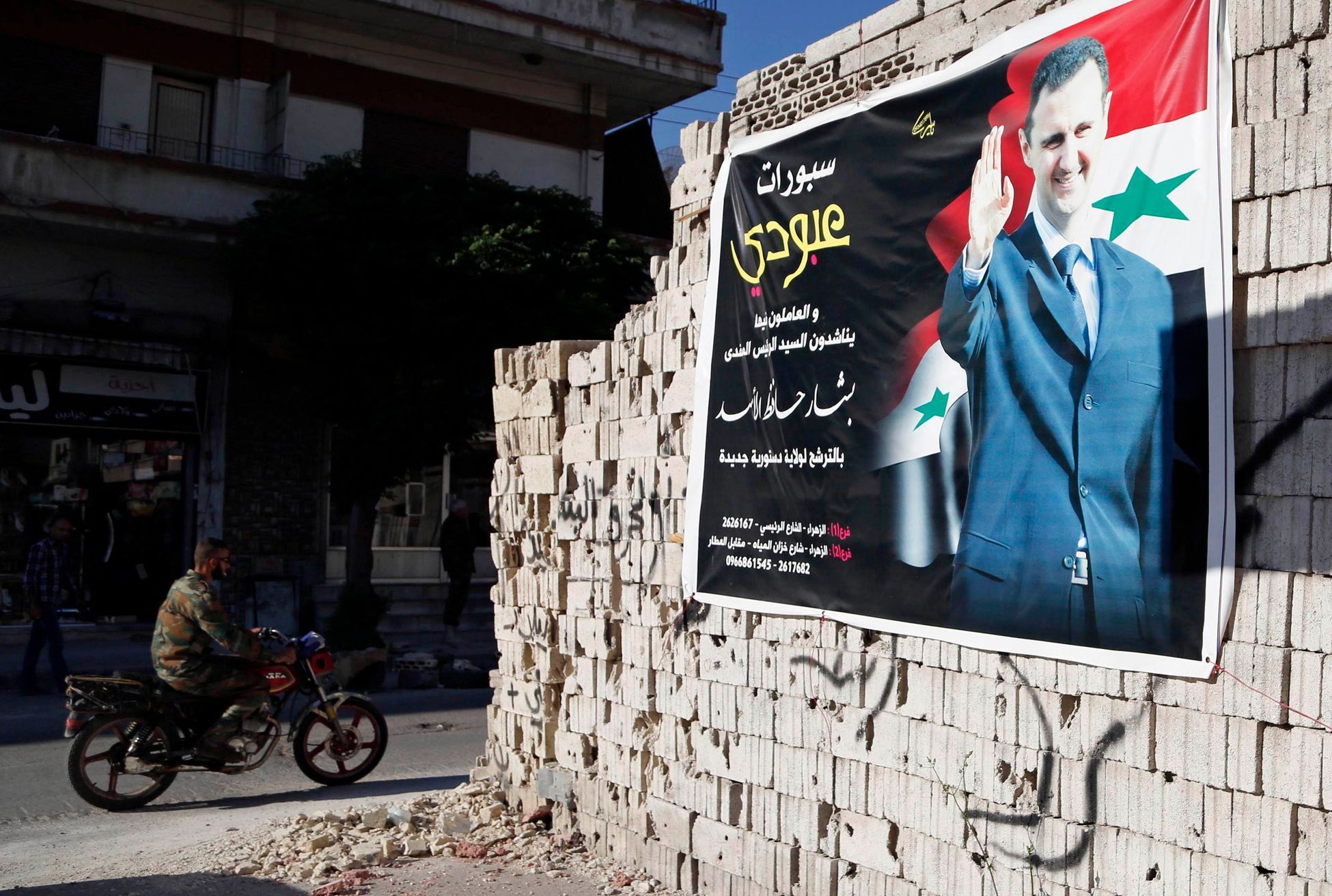 Man on a motorcycle rides past a poster depicting Syria's President Assad on a wall in the pro-government al-Zahraa neighbourhood in Homs