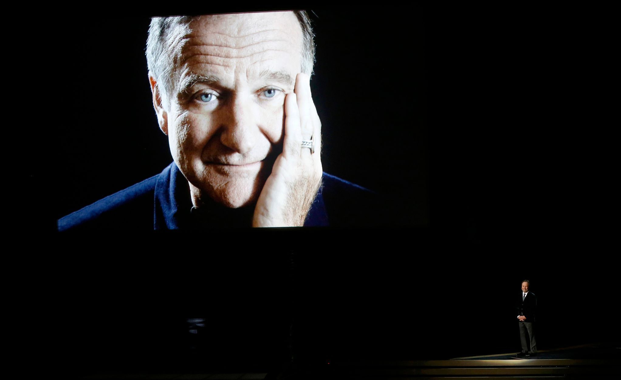 Billy Crystal takes the stage to pay tribute to Robin Williams, shown on a large screen, during the 66th Primetime Emmy Awards in Los Angeles