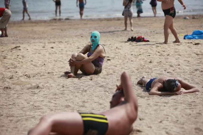 A woman, wearing a nylon mask, sits on the shore during her visit to a beach in Qingdao, Shandong province July 6, 2012. The mask, which was invented by a woman about seven years ago, is used to block the sun's rays. The mask is under mass production and is on sale at local swimwear stores. REUTERS/Aly Song (CHINA - Tags: SOCIETY ENVIRONMENT TRAVEL) Published: Čec. 6, 2012, 4:28 odp.