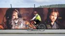 A man rides a bike along a fence hung with large format hoardings of J. R. R. Tolkien characters from The Hobbit movie in Wellington November 27, 2012. New Zealand's capital city was rushing to complete its transformation into a haven for hairy feet and pointed ears on Tuesday as stars jetted in for the long-awaited world premiere of the first movie of the Hobbit trilogy. REUTERS/Mark Coote (NEW ZEALAND - Tags: ENTERTAINMENT TRANSPORT) Published: Lis. 27, 2012, 3:07 dop.