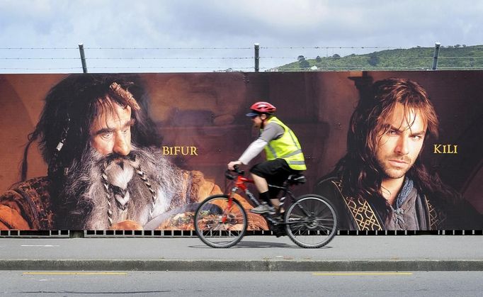 A man rides a bike along a fence hung with large format hoardings of J. R. R. Tolkien characters from The Hobbit movie in Wellington November 27, 2012. New Zealand's capital city was rushing to complete its transformation into a haven for hairy feet and pointed ears on Tuesday as stars jetted in for the long-awaited world premiere of the first movie of the Hobbit trilogy. REUTERS/Mark Coote (NEW ZEALAND - Tags: ENTERTAINMENT TRANSPORT) Published: Lis. 27, 2012, 3:07 dop.