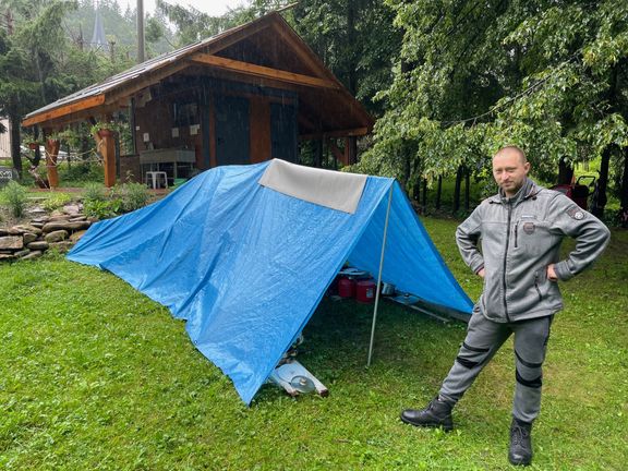 Václav u svého stanu v tábořišti Salajka. Jeho dvě děti si hrají uvnitř, v improvizované předsíňce skladuje nádobí a vařič. Byť silně prší, odejít nechce.