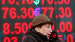 Žena mluví do telefonu před tabulí se směnnými kurzy rublu.