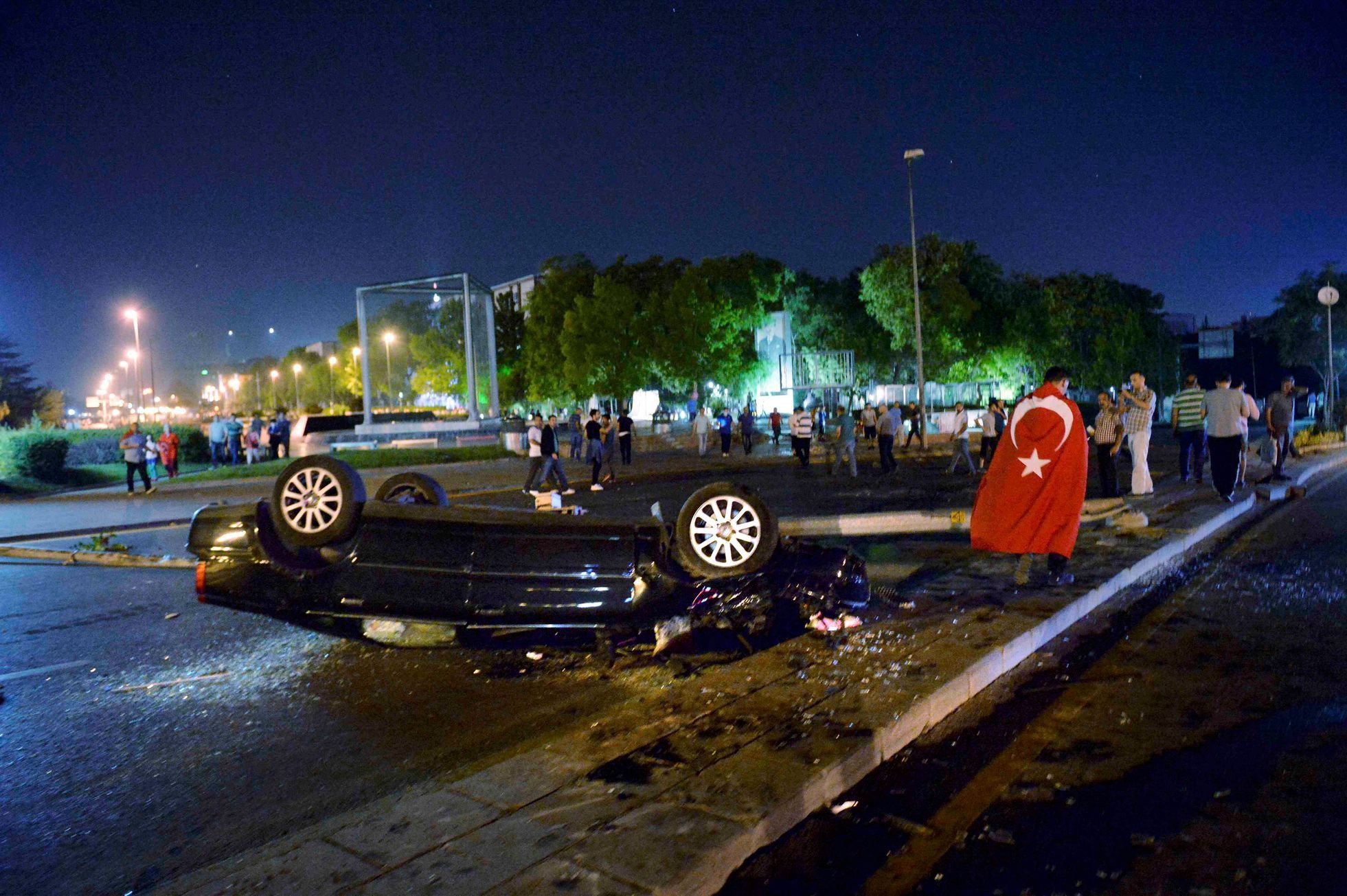 Muž zahalený do turecké vlajky prochází kolem převráceného auta v Ankaře