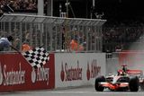 Lewis Hamilton s McLarenem protíná cílovou pásku Velké ceny Británie v Silverstonu.