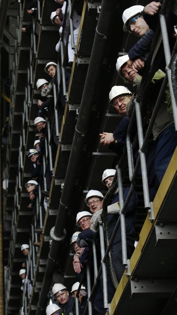 Workers watch as the forward section of the aircraft carrier HMS Queen Elizabeth is moved onto a barge at HM Naval Base in Portsmouth, southern England May 14, 2012. The hull will be transported by a sea going barge to Rosyth in Scotland where the ship will be assembled in dry dock. REUTERS/Luke MacGregor (BRITAIN - Tags: BUSINESS EMPLOYMENT MILITARY) Published: Kvě. 14, 2012, 2:30 odp.