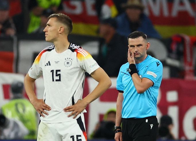 Rozhodčí Michael Oliver poslouchá pokyny, aby se při utkání Německo - Dánsko šel podívat na video