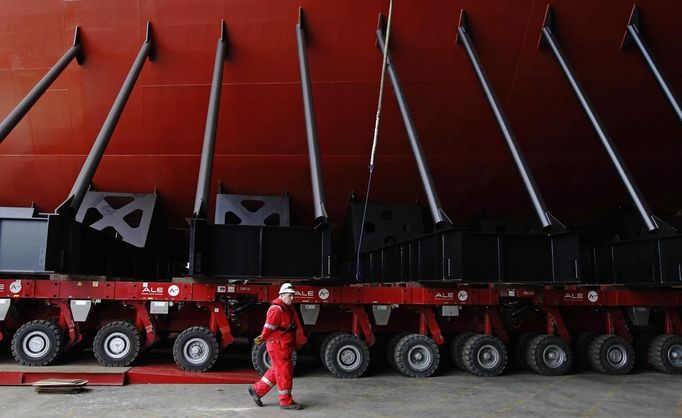 A worker passes the supports of the forward section of the aircraft carrier HMS Queen Elizabeth as it is moved onto a barge at HM Naval Base in Portsmouth, southern England May 14, 2012. The hull will be transported by a sea going barge to Rosyth in Scotland where the ship will be assembled in dry dock. REUTERS/Luke MacGregor (BRITAIN - Tags: BUSINESS EMPLOYMENT MILITARY) Published: Kvě. 14, 2012, 2:50 odp.