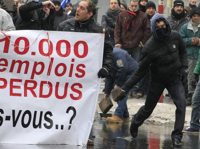 An Arcelor Mittal worker from Liege throws a stone next to a banner reading "10,000 jobs lost", during a demonstration outside Prime Minister Elio Di Rupo's office where a political meeting is taking place, in Brussels January 25, 2013. ArcelorMittal, the world's largest steel producer, plans to shut a coke plant and six fininishing lines at its site in Liege Belgium, affecting 1,300 employees, the group said on Thursday. REUTERS/Yves Herman (BELGIUM - Tags: BUSINESS CIVIL UNREST BUSINESS EMPLOYMENT) Published: Led. 25, 2013, 12:22 odp.