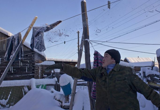 Igor Vinokurov, 35, knocks snow and ice off a frozen washing line in the village of Oymyakon, in the Republic of Sakha, northeast Russia, January 26, 2013. The coldest temperatures in the northern hemisphere have been recorded in the Oymyakon valley, where according to the United Kingdom Met Office a temperature of -67.8 degrees Celsius (-90 degrees Fahrenheit) was registered in 1933 - the coldest on record in the northern hemisphere since the beginning of the 20th century. Yet despite the harsh climate, people live in the valley, and the area is equipped with schools, a post office, a bank, and even an airport runway (albeit open only in the summer). Picture taken January 26, 2013. REUTERS/Maxim Shemetov (RUSSIA - Tags: SOCIETY ENVIRONMENT) ATTENTION EDITORS: PICTURE 13 OF 27 FOR PACKAGE 'THE POLE OF COLD' SEARCH 'MAXIM COLD' FOR ALL IMAGES Published: Úno. 18, 2013, 11:25 dop.