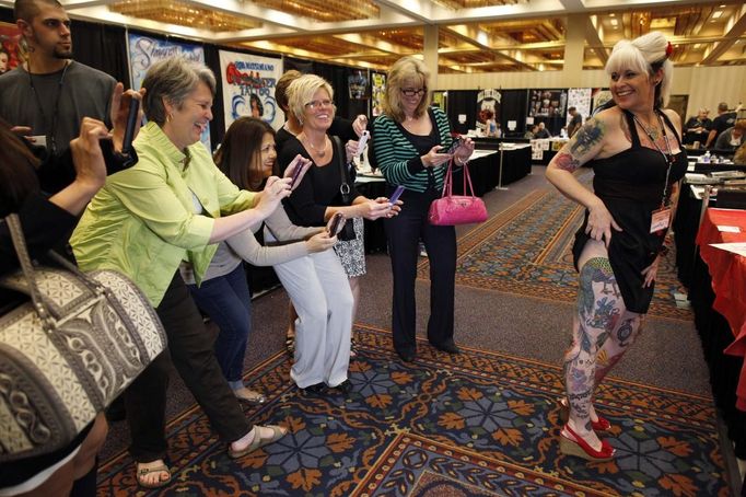 A group of women from an adjacent quilting fair sneak into the National Tattoo Association Convention in Cincinnati to take a picture of a heavily-tattooed convention-goer in Ohio April 14, 2012. The hobby of collecting tattoos has exploded into the mainstream of society with tattoo conventions and festivals held year-round across the United States. Picture taken April 14, 2012. REUTERS/Larry Downing (UNITED STATES - Tags: SOCIETY) ATTENTION EDITORS PICTURE 16 OF 31 FOR PACKAGE 'ADDICTED TO THE NEEDLE' TO FIND ALL PICTURES SEARCH 'ADDICTED NEEDLE' Published: Čer. 29, 2012, 12:59 odp.