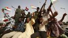 People wave Sudanese flags as they ride a military vehicle along with soldiers, during a celebration march outside the Defence Ministry in Khartoum