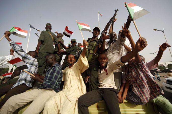 People wave Sudanese flags as they ride a military vehicle along with soldiers, during a celebration march outside the Defence Ministry in Khartoum