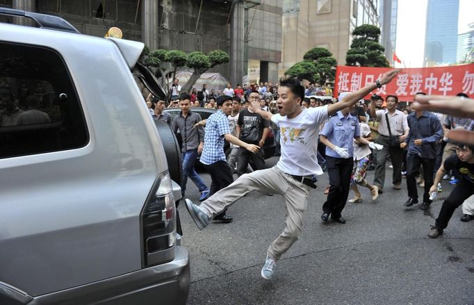 A demonstrator kicks a Japanese-brand car during a protest in Chongqing, September 15, 2012. Thousands of Chinese besieged the Japanese embassy in Beijing on Saturday, hurling rocks, eggs and bottles with protests reported in other major cities in China amid growing tension between Asia's two biggest economies over a group of disputed islands. Part of the Chinese characters on the banner (R) reads, "Boycott Japanese products, love my China." REUTERS/Stringer (CHINA - Tags: POLITICS) CHINA OUT. NO COMMERCIAL OR EDITORIAL SALES IN CHINA