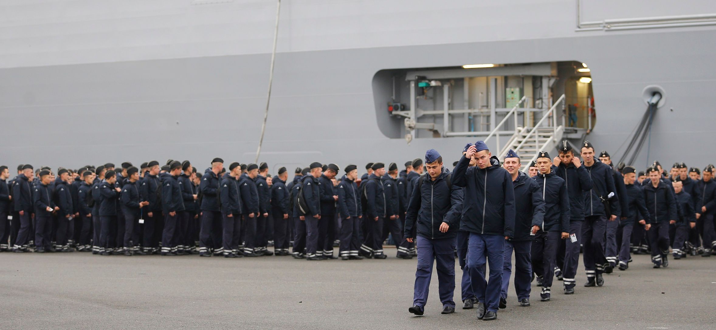 Russian sailors walk in front of the Mistral-class helicopter carrier Vladivostok at the STX Les Chantiers de l'Atlantique shipyard site in Saint-Nazaire