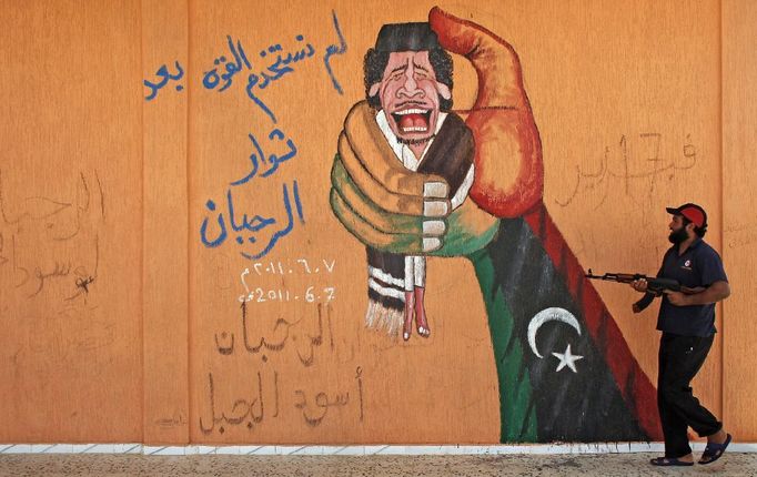 Libyjský rebel jde kolem graffiti znázorňujícího Muammara Kaddáfího, jehož věrní definitivně ztratili na konci srpna kontrolu nad Tripolisem a část jeho rodiny uprchla do Alžírska.