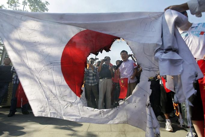 Protesters laugh and take pictures next to a burned Japanese national flag during an anti-Japan protest in Wuhan, Hubei province September 16, 2012. Angry anti-Japan protesters took to the streets of Chinese cities for a second day on Sunday, with Japan's prime minister urging Beijing to protect his country's companies and diplomatic buildings from fresh assaults over a territorial dispute. REUTERS/Stringer (CHINA - Tags: CIVIL UNREST POLITICS TPX IMAGES OF THE DAY) CHINA OUT. NO COMMERCIAL OR EDITORIAL SALES IN CHINA