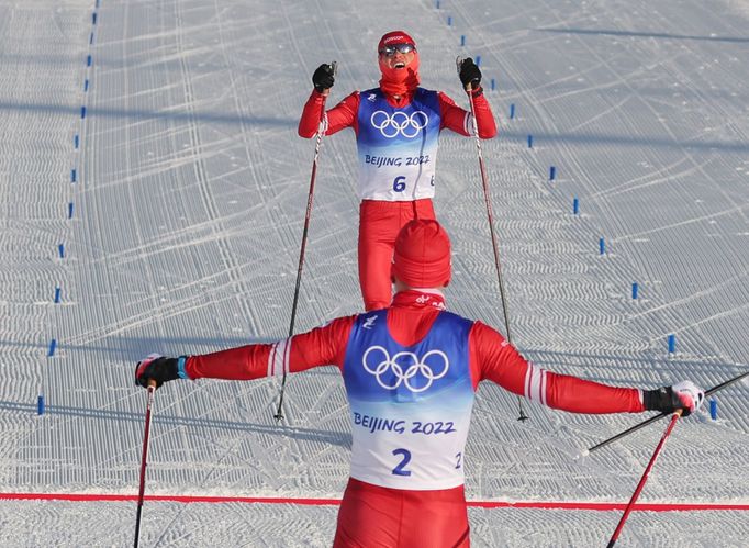 Alexander Bolšunov (zády) a Denis Spicov slaví vítězství ve skiatlonu na olympiádě v Pekingu 2022