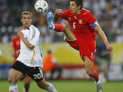 Jacek Bak z Polska (v červeném) odkopává míč, vzadu je německý hráč Lukas Podolski.