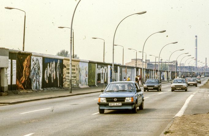 Berlínská zeď s malbami podél Mühlenstrasse, známá jako East Side Gallery, s projíždějícími automobily. Rok 1990