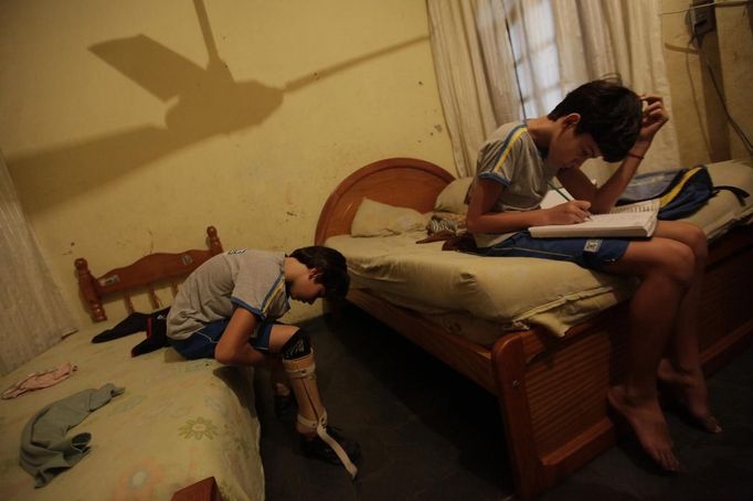 Gabriel Muniz, 11, puts on his prosthesis as his brother Mateus studies at home in Campos dos Goytacazes, 274 kilometres (170 miles) northeast of Rio de Janeiro August 23, 2012. Despite being born with malformation of his feet, fourth grader Gabriel puts in hours into soccer everyday in his neighbourhood. He aspires to be a professional soccer player just like his idol Argentina's Lionel Messi of Barcelona FC. REUTERS/Ricardo Moraes (BRAZIL - Tags: SPORT SOCCER SOCIETY HEALTH TPX IMAGES OF THE DAY) Published: Srp. 24, 2012, 2:25 dop.