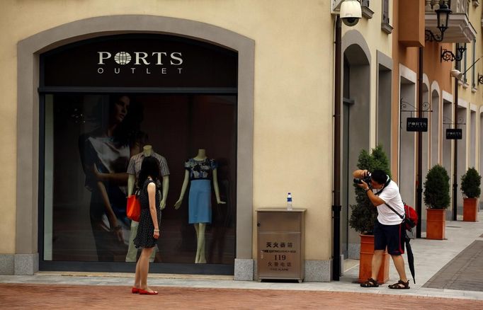 A man takes a photograph of a woman outside a fashion store in the Florentia Village in the district of Wuqing, located on the outskirts of the city of Tianjin June 13, 2012. The shopping center, which covers an area of some 200,000 square meters, was constructed on a former corn field at an estimated cost of US$220 million and copies old Italian-style architecture with Florentine arcades, a grand canal, bridges, and a building that resembles a Roman Coliseum. REUTERS/David Gray (CHINA - Tags: SOCIETY BUSINESS) Published: Čer. 13, 2012, 5:52 odp.