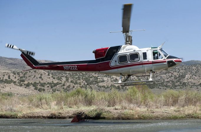 A helicopter scoops water from a river as fire fighters battle the Topaz Ranch Estates fire in Wellington, Nevada May 24, 2012. Lighter winds and higher humidity helped crews' efforts to curb the Topaz Ranch Estates wildfire that has razed more than 9 square miles (23 square km) of brush south of Carson City, charring two homes and more than a dozen outbuildings. REUTERS/James Glover II (UNITED STATES - Tags: DISASTER ENVIRONMENT) Published: Kvě. 25, 2012, 1:52 dop.