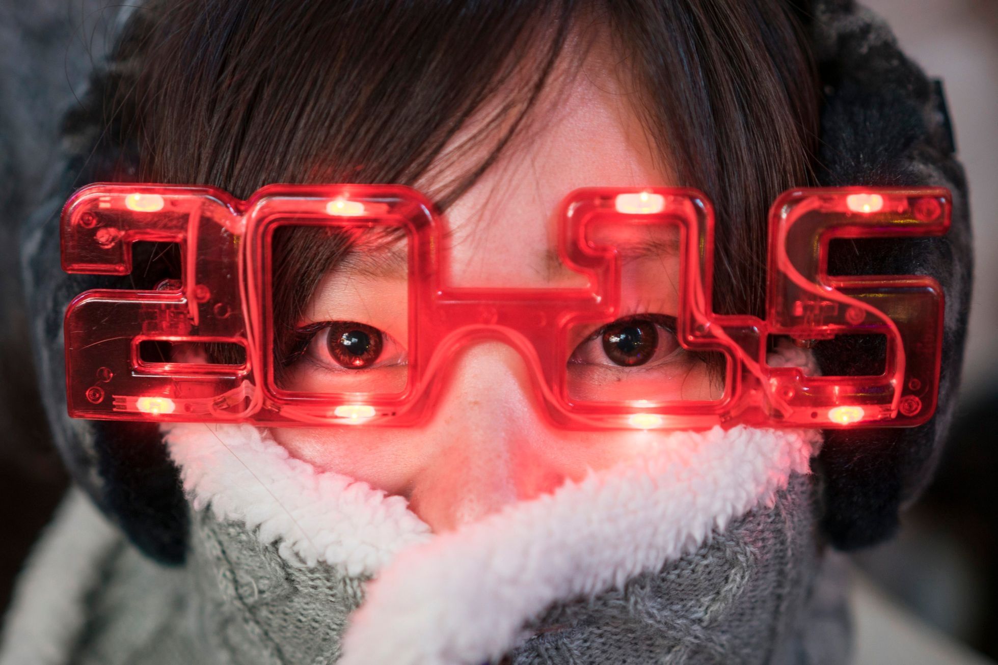 A woman sports 2015 glasses while taking cover from the cold weather during New Year's Eve celebrations in Times Square, New York