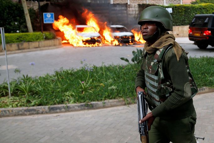 A policeman runs past burning cars at the scene where explosions and gunshots were heard at the Dusit hotel compound, in Nairobi, Kenya