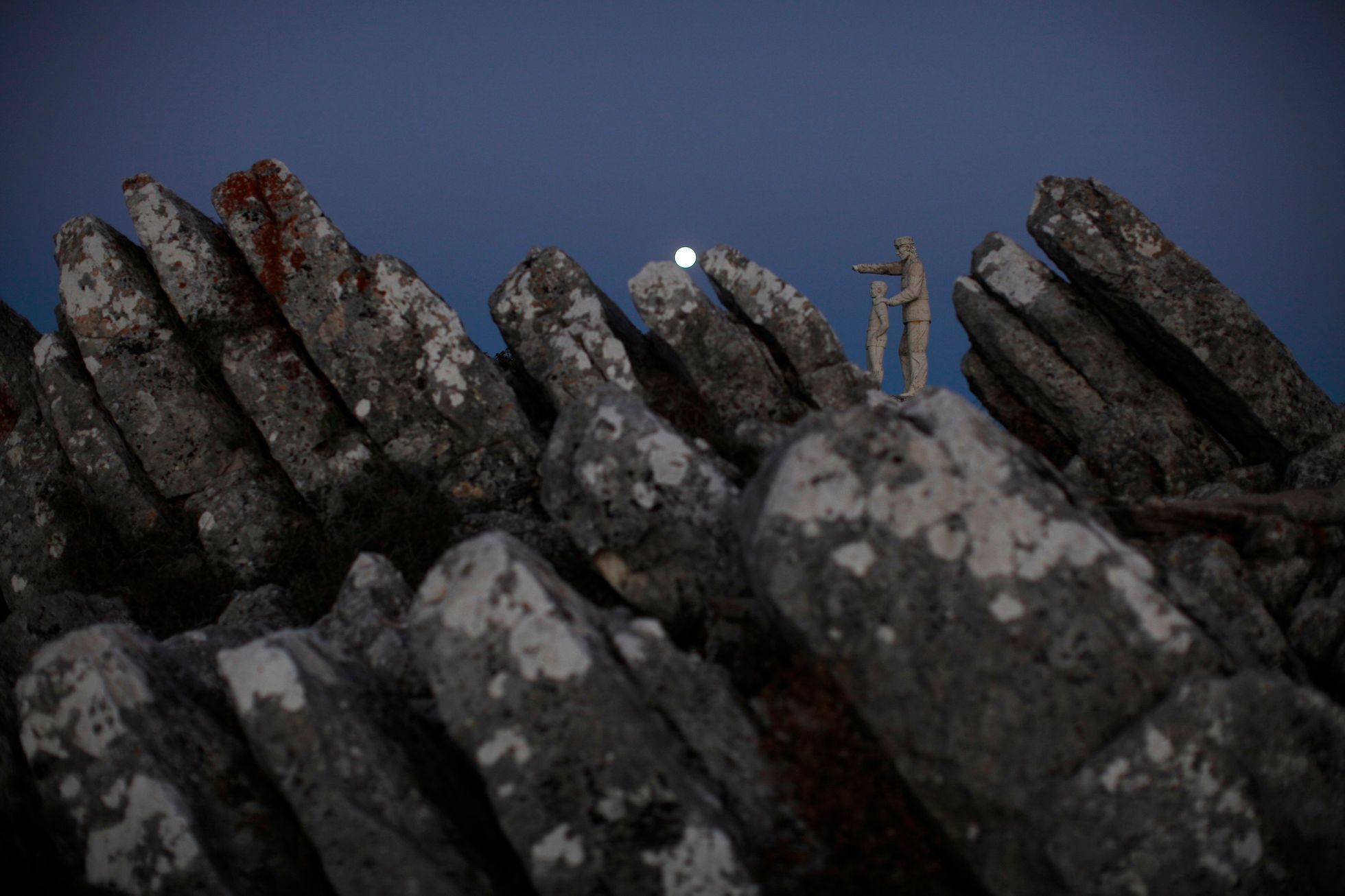 A view of a monument dedicated to forest rangers as the supermoon sets over the horizon at dawn at a nature park and biosphere reserve near Malaga