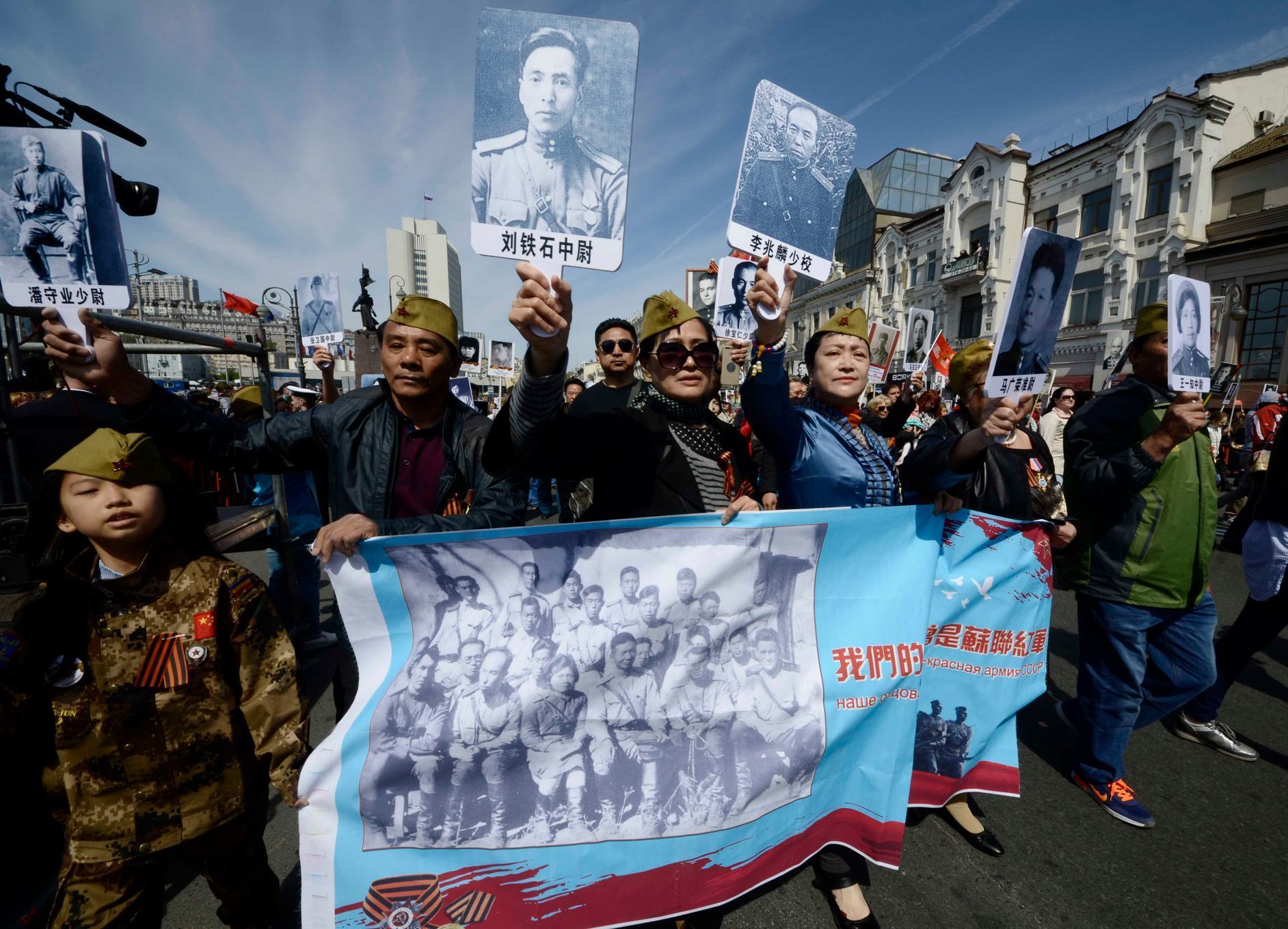 Lidé z čínské provincie Chej-lung-ťiang drží na pochodu ve Vladivostoku fotky svých příbuzných, kteří bojovali v druhé světové válce.