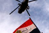 Egypťan zvedá vlajku k nebi, na kterém přelétá vojenská helikoptéra.