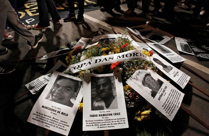 Flowers with a banner reading &quot;World Cup of deaths&quot; draped across them are placed on the ground next to pictures of workers who died during construction of Worl