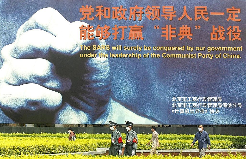 Masked security guards walk past a SARS propaganda billboard, 20 May 2003 in Beijing. Chinese health officials announced today that the outbreak of the Severe Acute Respiratory Syndrome (SARS) virus in the Chinese capital is "effectively contained", but cautioned an arduous task remained ahead.