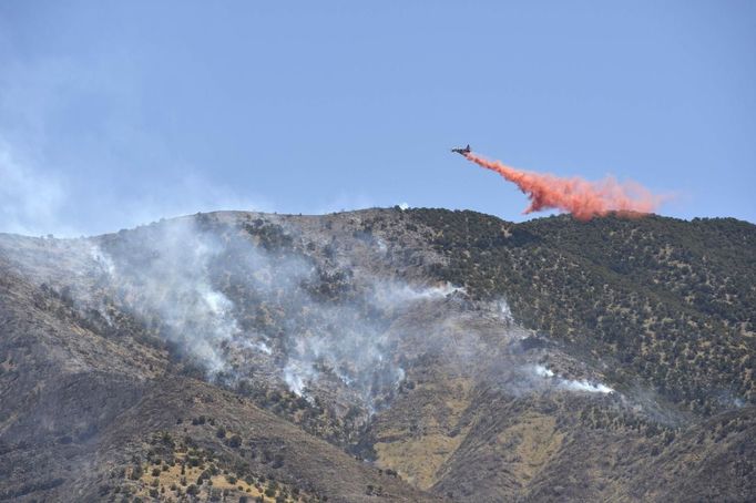 An airplane drops fire retardant along a mountain ridge near Eagle Mountain, Utah, June 23, 2012. A raging Utah brush fire ignited by target shooting in dry grass has forced some 8,000 people from their homes in two small communities since June 22 as high winds fanned flames toward a nearby explosives factory, authorities said. REUTERS/Jeff McGrath (UNITED STATES - Tags: ENVIRONMENT DISASTER) Published: Čer. 23, 2012, 8:50 odp.