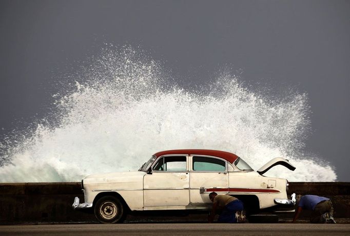 Muži vyměňují pneumatiku u jejich auta na nábřeží během příboje. Foceno v Havaně dne 7. listopadu 2011. REUTERS/Desmond Boylan