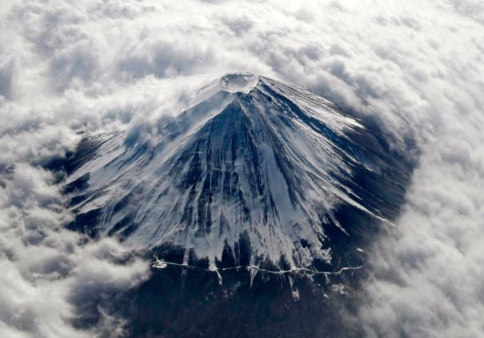 Letecký snímek. Hora Fuji (3 776 m) je nejvyšší horou Japonska. Nachází se na hranici mezi prefekturami Šizuoka a Jamanaši asi 100 km na západ od Tokia. Na tomto snímku je pokryta sněhem a zahalena do oblačné peřiny.