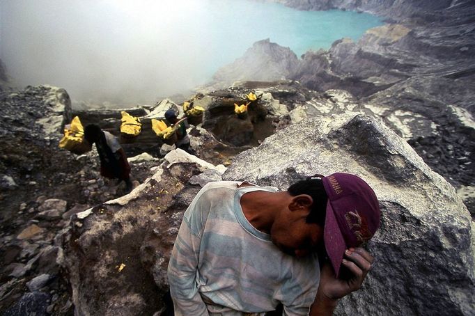 Indonesia - Living Dangerously A miners rests on a rock, exhausted from the climb up from the crater carrying between 80 and 110kg of sulfur from the sulfur mine on the Ijen Crater volcano in Indonesia. The workers at the mine have no protection against the toxic sulfur and carry heavy loads up from the crater to the valley below the volcano several times each day. A blue sulfur acid lake is filling up the crater.