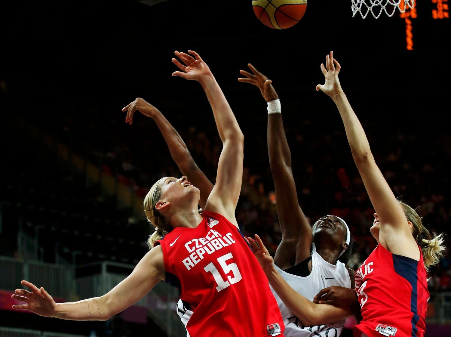České basketbalistky Eva Vítečková a Petra Kulichová vyskakují nad Angolku Luisu Tomasovou v utkání skupiny A na OH 2012 v Londýně.