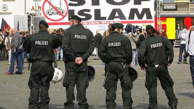 Policisté stojí před obřím transparentem setkání islamofobů.