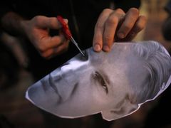 Assangeho fanoušek vystřihuje v masce šéfa WikiLeaks, kterou si chce nasadit, otvory pro oči