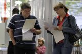 Lidé studují hlasovací lístky ve volební místnosti.
