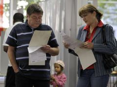 Lidé studují hlasovací lístky ve volební místnosti.